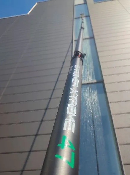Teleskopstange mit Aufschrift 'EMEX XTREME 47' vor einer hohen Glasfassade im Außenbereich