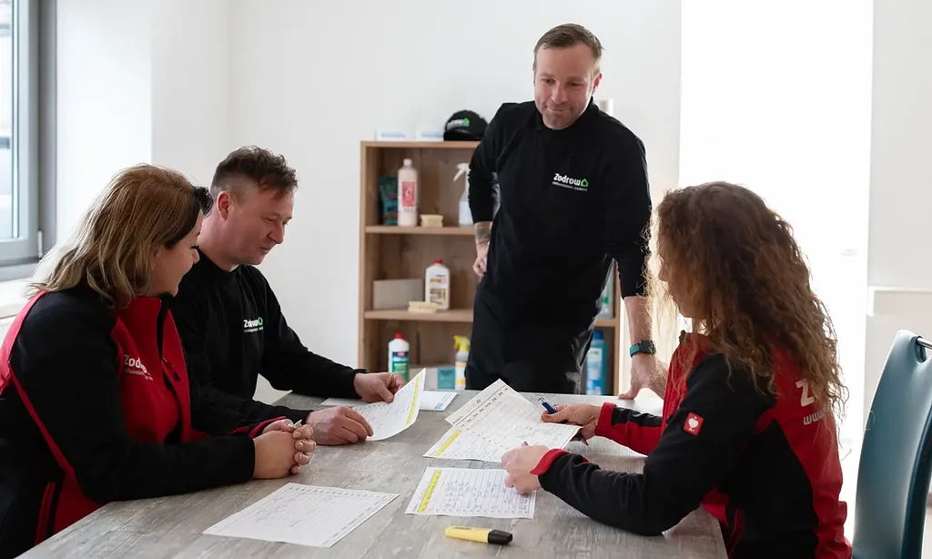 Vier Personen sitzen an einem Tisch und besprechen handschriftliche Notizen in einem hellen Büro