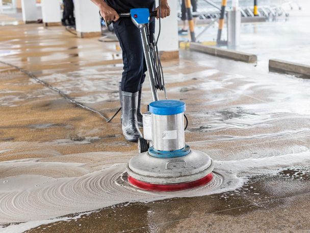 Worker cleaning sand wash exterior walkway using polishing machine and chemical or acid