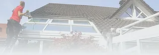 Person reinigt Fenster eines modernen Glaswintergartens an einem Haus mit Satteldach