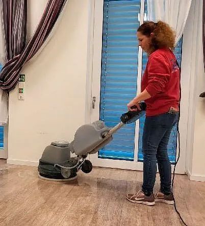 Person reinigt Holzboden mit elektrischer Scheuermaschine in hellem Raum mit blauen Fensterläden