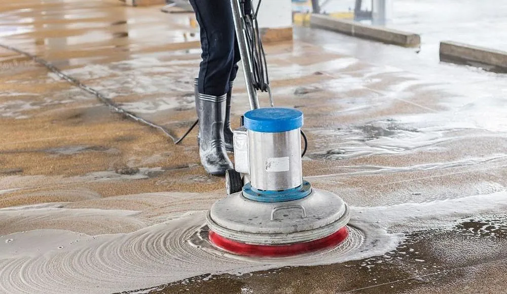 Person reinigt Boden mit rotierender Scheuermaschine und Schaum auf Betonboden